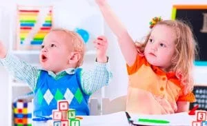 a boy and girl raise their hands while sitting in chairs