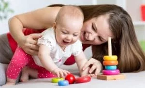 a mother helps her infant daughter play with colorful shape blocks