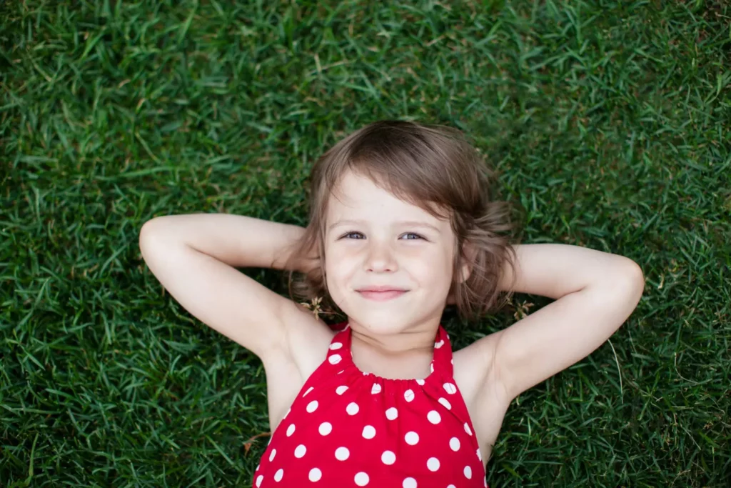 young girl sits in bed of grass smiling up at camera