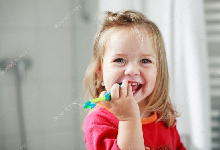 toddler girl smiles at camera with toothbrush in hand