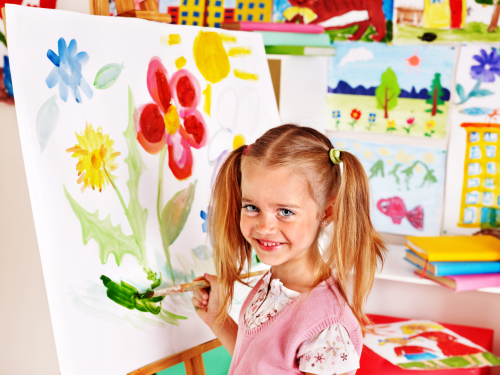 picture of a girl painting on an easel smiling at the camera in art class